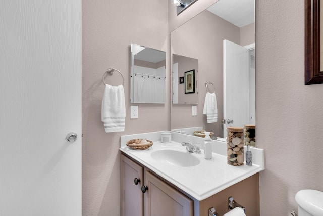 bathroom with vanity, a textured wall, and toilet