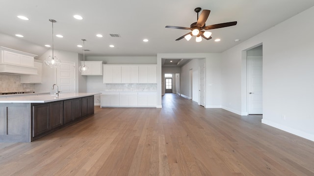 7313 Wayward Wind Dr, Fort Worth, TX 76179 - kitchen with backsplash, light countertops, light wood-style floors, a center island with sink, and white cabinetry