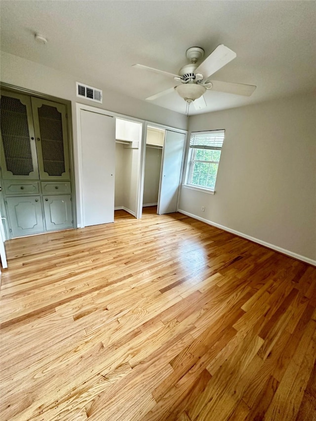 unfurnished bedroom with light wood finished floors, two closets, a ceiling fan, baseboards, and visible vents