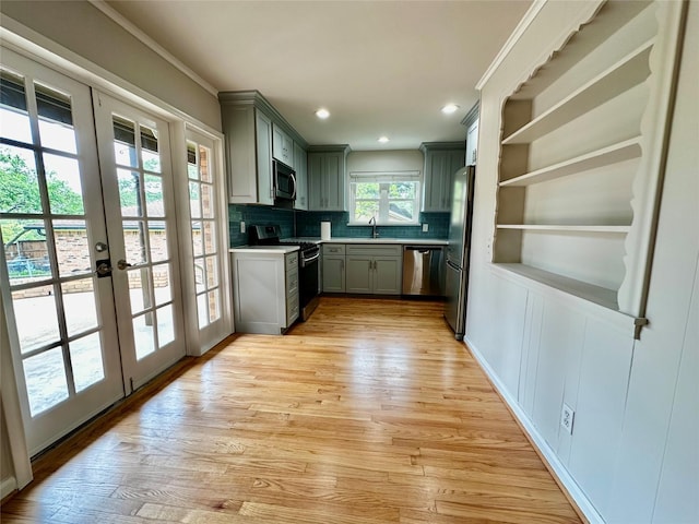 kitchen featuring appliances with stainless steel finishes, a sink, gray cabinets, light wood-type flooring, and tasteful backsplash