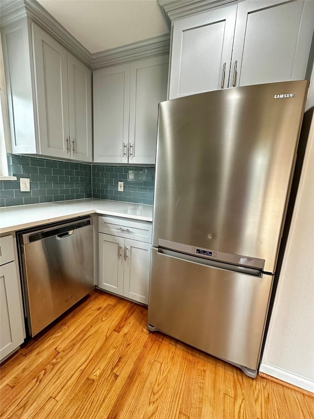 kitchen featuring light countertops, backsplash, stainless steel appliances, and light wood-type flooring