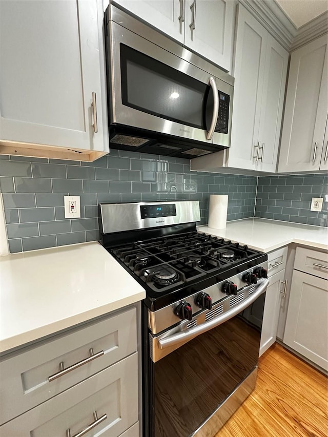 kitchen featuring light countertops, light wood finished floors, backsplash, and stainless steel appliances