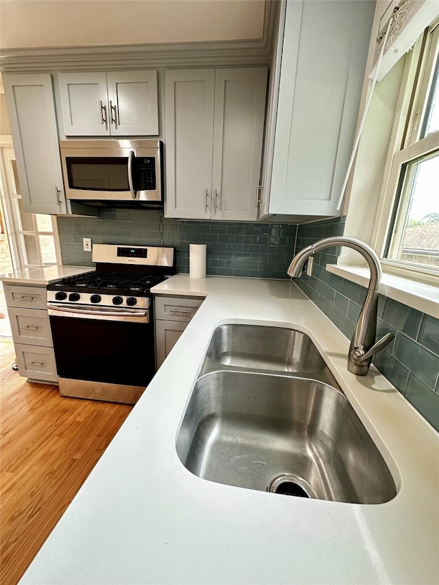 kitchen with stainless steel appliances, gray cabinetry, a sink, and light wood-type flooring