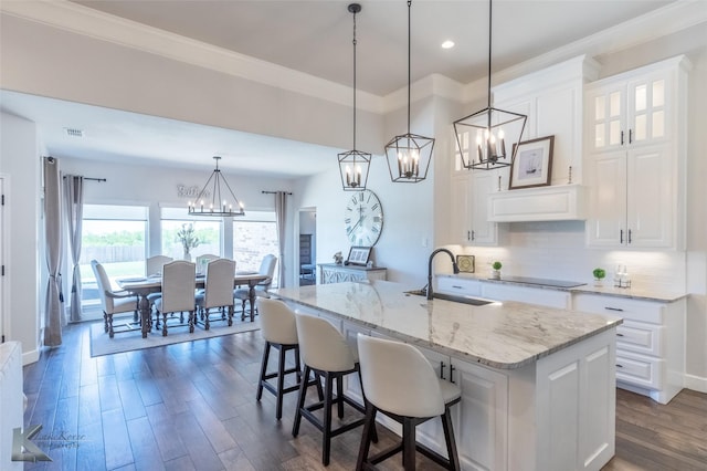 kitchen with a sink, light stone counters, dark wood-style floors, a notable chandelier, and ornamental molding