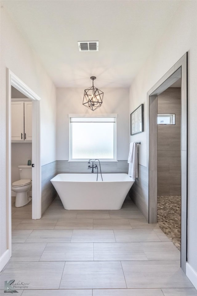 bathroom featuring visible vents, a freestanding tub, tile walls, tile patterned floors, and toilet