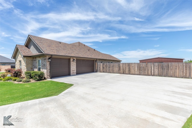 view of side of home with driveway, roof with shingles, a garage, fence, and a yard