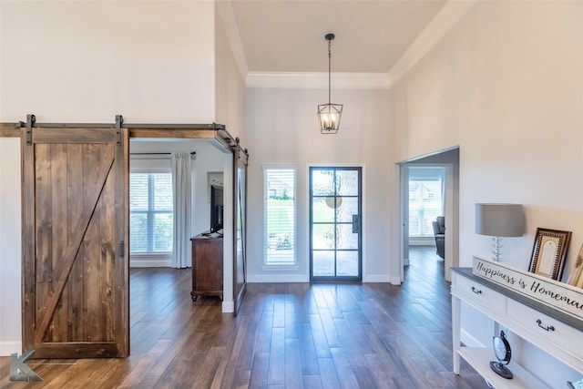 foyer entrance with a barn door, baseboards, wood finished floors, a towering ceiling, and ornamental molding