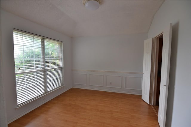 empty room featuring vaulted ceiling, wainscoting, and light wood-style floors