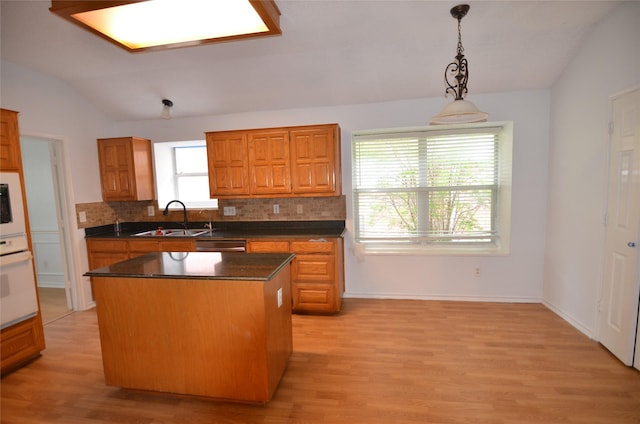 kitchen featuring tasteful backsplash, vaulted ceiling, light wood-type flooring, white oven, and a sink