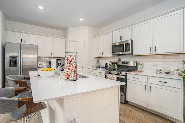 kitchen featuring a kitchen island with sink, backsplash, appliances with stainless steel finishes, light countertops, and light wood-style floors