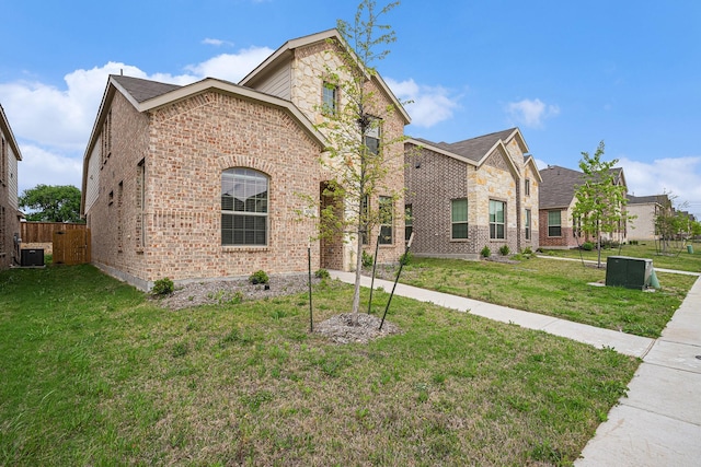 view of front facade featuring brick siding, fence, a front yard, and cooling unit