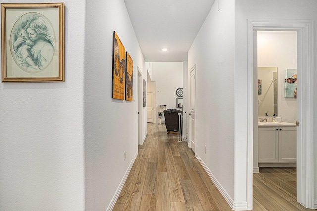 corridor featuring baseboards, a sink, light wood-style flooring, and recessed lighting