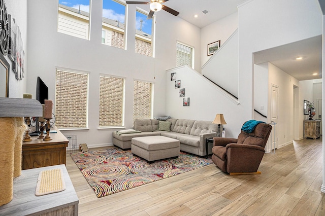 living area with stairs, a ceiling fan, baseboards, wood finished floors, and a towering ceiling