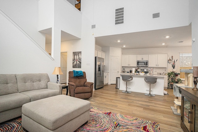 living area featuring visible vents, recessed lighting, light wood-style flooring, and a towering ceiling