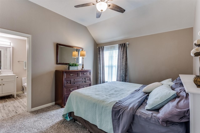 bedroom with baseboards, ensuite bathroom, light colored carpet, a ceiling fan, and vaulted ceiling