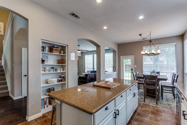 kitchen featuring visible vents, light stone countertops, a center island, white cabinets, and built in shelves