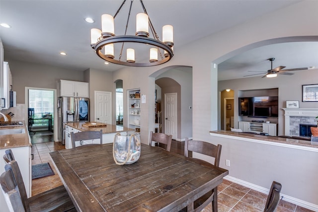 dining space featuring arched walkways, ceiling fan with notable chandelier, recessed lighting, baseboards, and dark tile patterned floors