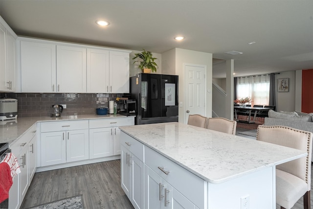 kitchen with light stone countertops, open floor plan, a center island, backsplash, and black fridge