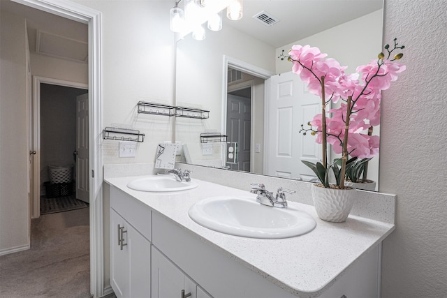 bathroom with double vanity, a textured wall, visible vents, and a sink