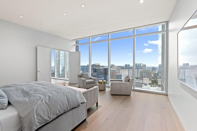 bedroom featuring expansive windows, a city view, light wood finished floors, and baseboards