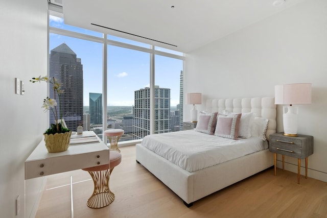 bedroom featuring a view of city, expansive windows, and light wood-style flooring