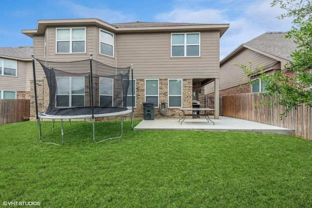 back of house featuring a trampoline, a lawn, brick siding, a fenced backyard, and a patio