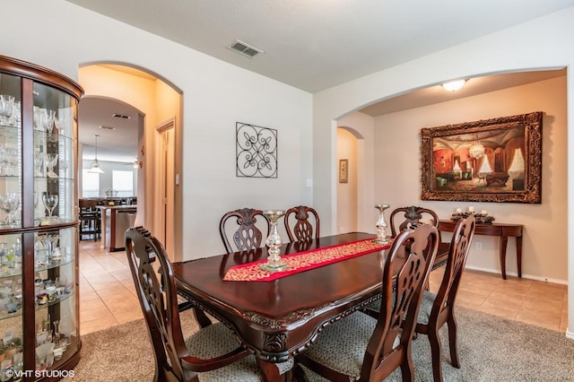 dining area with light tile patterned floors, arched walkways, light carpet, and visible vents