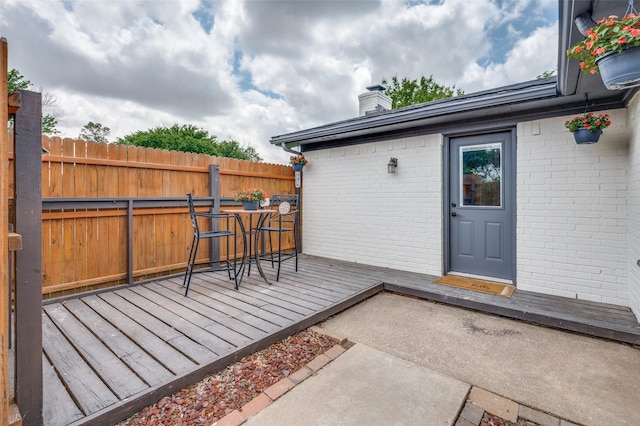 doorway to property featuring brick siding, fence, a chimney, and a wooden deck