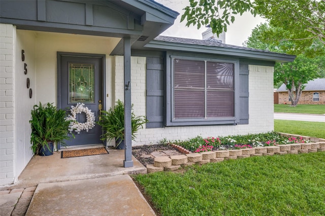 doorway to property with brick siding, a lawn, and a chimney