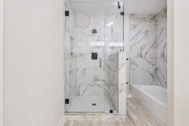 bathroom featuring a garden tub, a marble finish shower, and wood finished floors