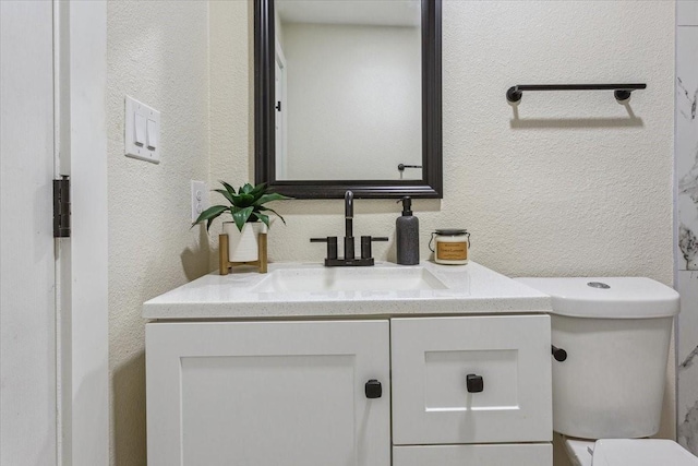 half bath featuring toilet, a textured wall, and vanity