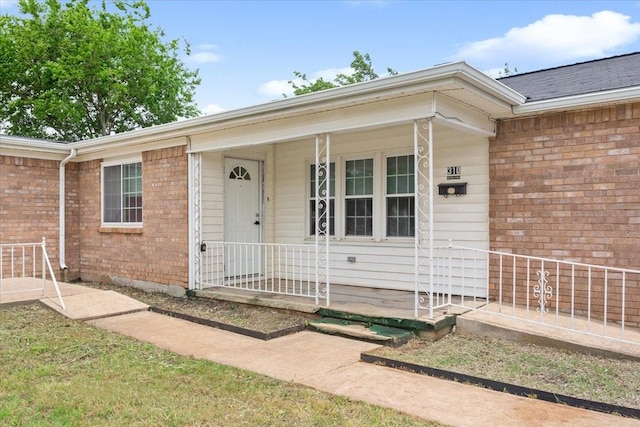 doorway to property featuring a porch and brick siding