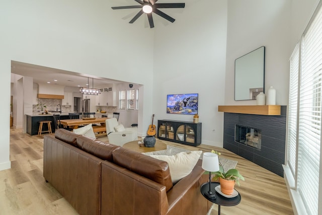 12472 Jack Pine Ct, Frisco, TX 75035 - living area with a towering ceiling, a ceiling fan, a tiled fireplace, light wood-style flooring, and baseboards