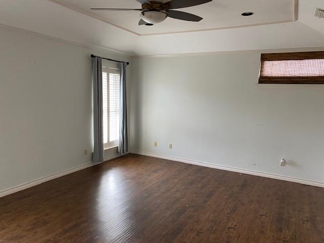unfurnished room with ceiling fan, visible vents, a raised ceiling, baseboards, and dark wood-style floors