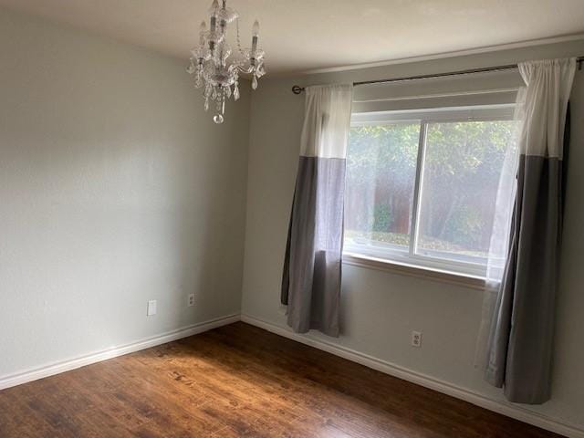 spare room with baseboards, an inviting chandelier, and wood finished floors