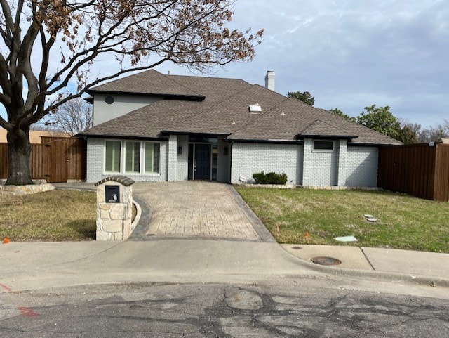 view of front of property with a chimney, roof with shingles, a front yard, brick siding, and fence