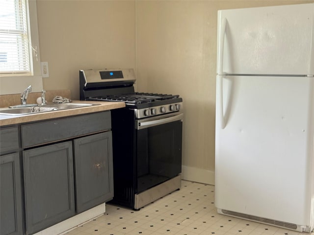 kitchen with gray cabinets, a sink, freestanding refrigerator, stainless steel range with gas cooktop, and light floors