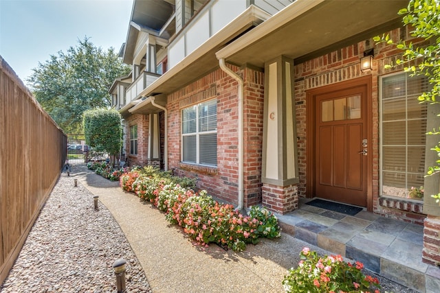 view of exterior entry with fence and brick siding