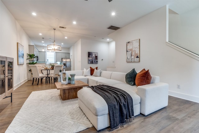 living room with visible vents, wood finished floors, baseboards, a notable chandelier, and recessed lighting