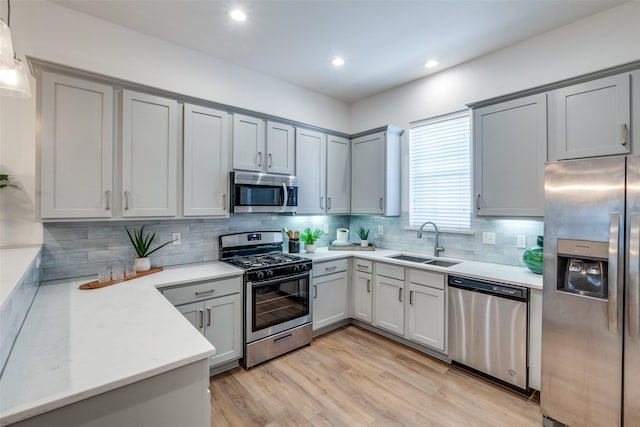 kitchen with light countertops, tasteful backsplash, a sink, gray cabinetry, and stainless steel appliances