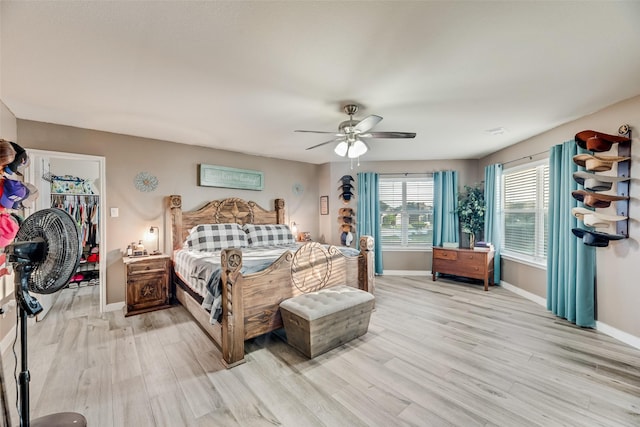 bedroom with a walk in closet, baseboards, and light wood-style flooring
