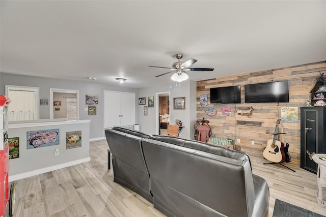 living room featuring wooden walls, ceiling fan, baseboards, and wood finished floors