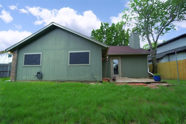 rear view of house featuring a yard, a deck, fence, and a chimney