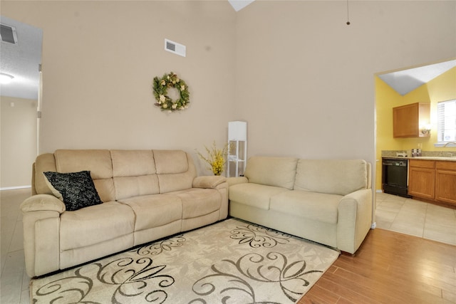 living room featuring high vaulted ceiling, light wood-type flooring, and visible vents