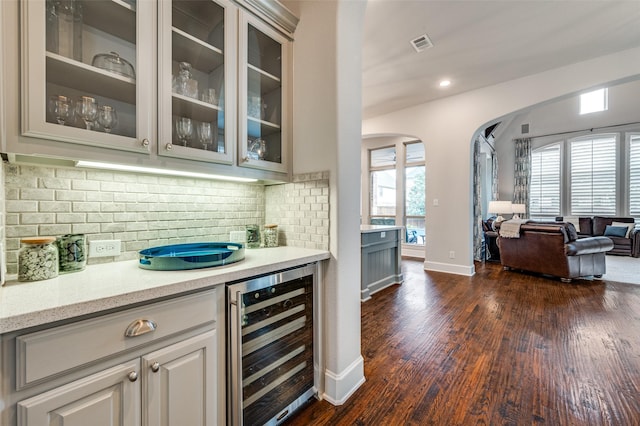 bar featuring backsplash, dark wood-style flooring, arched walkways, baseboards, and wine cooler