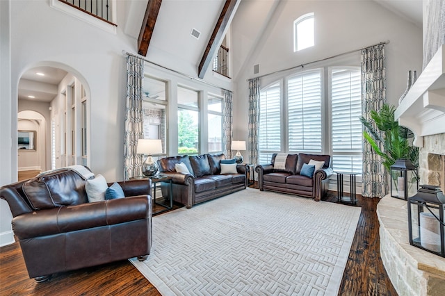 living area with visible vents, wood finished floors, beamed ceiling, high vaulted ceiling, and arched walkways