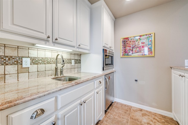 interior space with tasteful backsplash, a sink, baseboards, stainless steel microwave, and white cabinetry