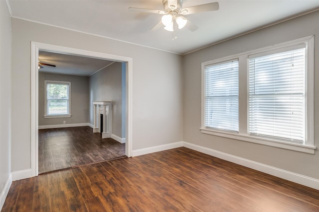 spare room featuring crown molding, a fireplace, baseboards, ceiling fan, and dark wood finished floors