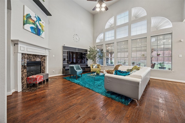 living area with a premium fireplace, a ceiling fan, baseboards, wood finished floors, and a towering ceiling