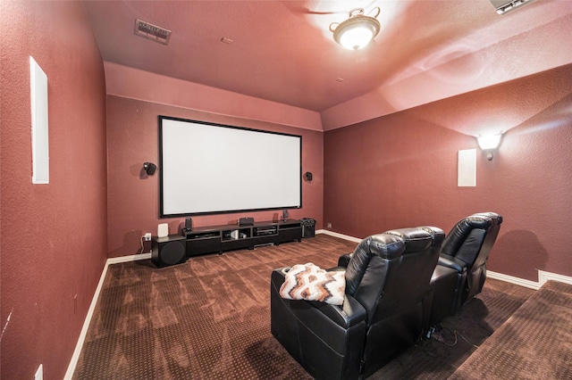 carpeted cinema featuring baseboards, visible vents, a textured wall, and vaulted ceiling
